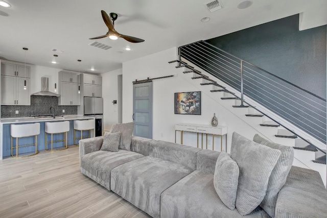 living area with a barn door, visible vents, ceiling fan, and stairway