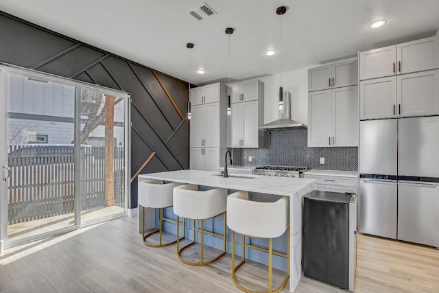 kitchen featuring visible vents, wall chimney range hood, appliances with stainless steel finishes, light wood-style floors, and a sink