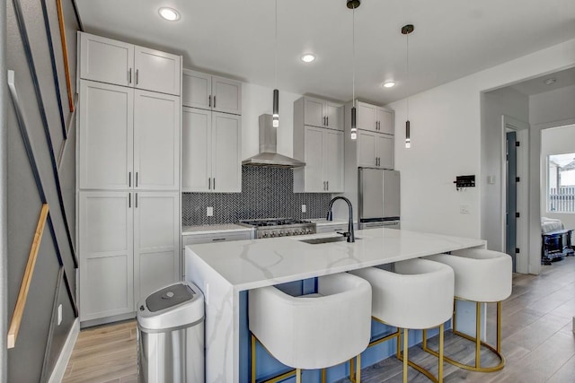 kitchen with light wood-type flooring, decorative backsplash, freestanding refrigerator, wall chimney exhaust hood, and a sink