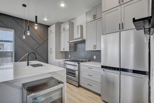 kitchen with light stone counters, decorative backsplash, appliances with stainless steel finishes, wall chimney exhaust hood, and a sink