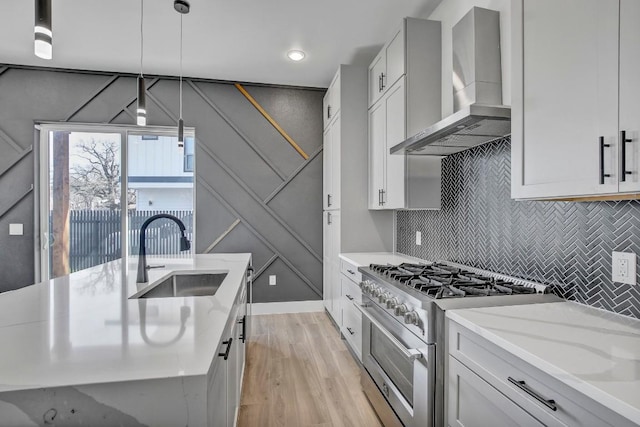 kitchen featuring light wood-type flooring, high end stainless steel range, a sink, tasteful backsplash, and wall chimney range hood