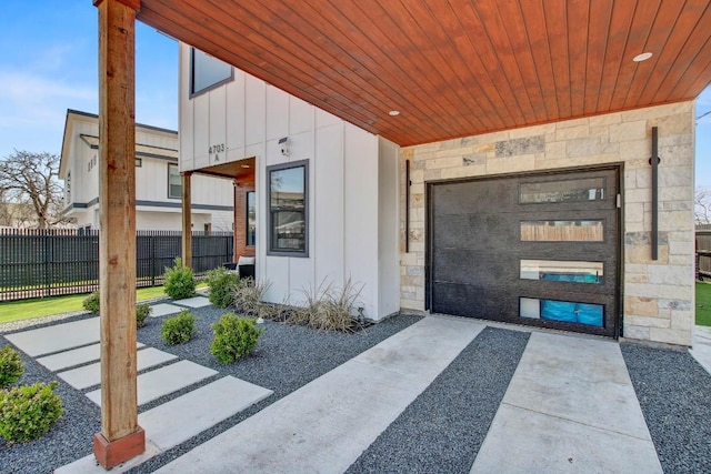 doorway to property with driveway, stone siding, fence, board and batten siding, and an attached garage