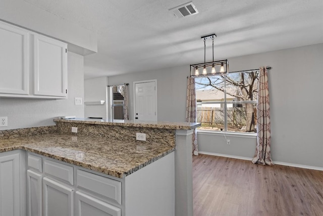 kitchen with visible vents, light stone counters, light wood-style flooring, a peninsula, and white cabinetry