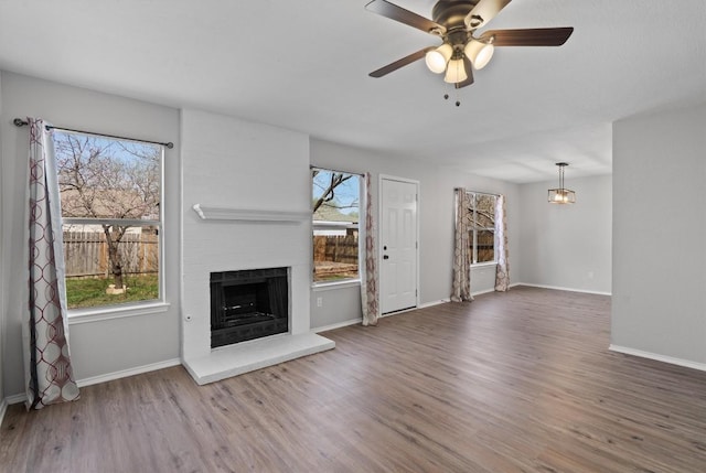 unfurnished living room with baseboards, a large fireplace, ceiling fan, and wood finished floors