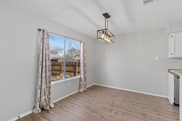 unfurnished dining area featuring a chandelier, visible vents, light wood-style flooring, and baseboards