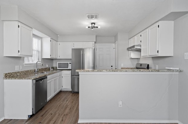 kitchen with light stone counters, a sink, under cabinet range hood, appliances with stainless steel finishes, and white cabinetry