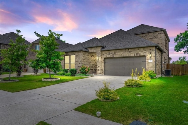 french provincial home with driveway, a yard, a shingled roof, a garage, and brick siding