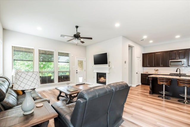 living area featuring light wood-type flooring, visible vents, a glass covered fireplace, recessed lighting, and ceiling fan