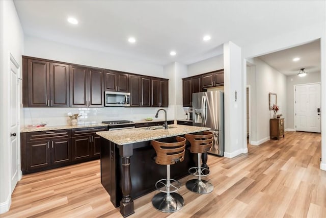 kitchen featuring light wood-type flooring, a center island with sink, a sink, light stone counters, and stainless steel appliances