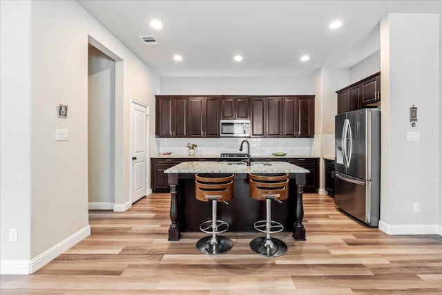 kitchen with visible vents, an island with sink, a sink, dark brown cabinetry, and appliances with stainless steel finishes