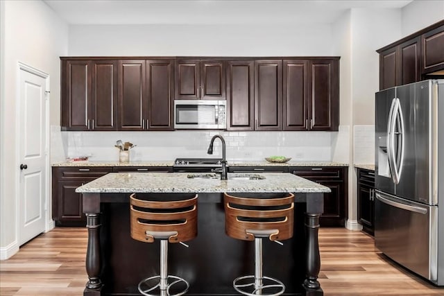 kitchen with backsplash, appliances with stainless steel finishes, light wood-style floors, and a sink