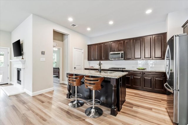 kitchen with a breakfast bar area, light stone counters, light wood-style flooring, a sink, and stainless steel appliances