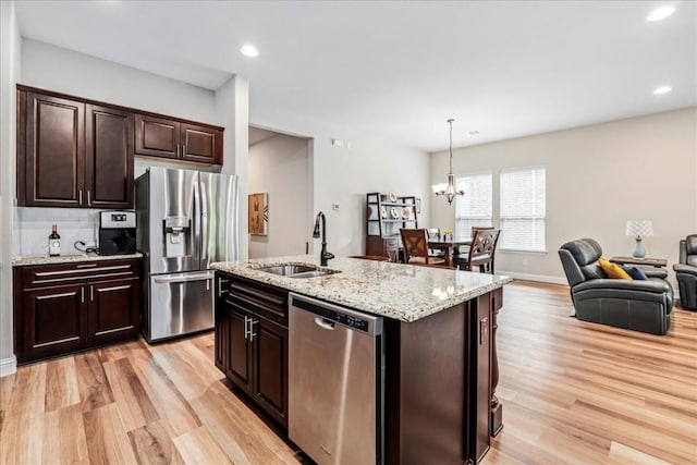 kitchen with appliances with stainless steel finishes, pendant lighting, light wood-type flooring, and a sink