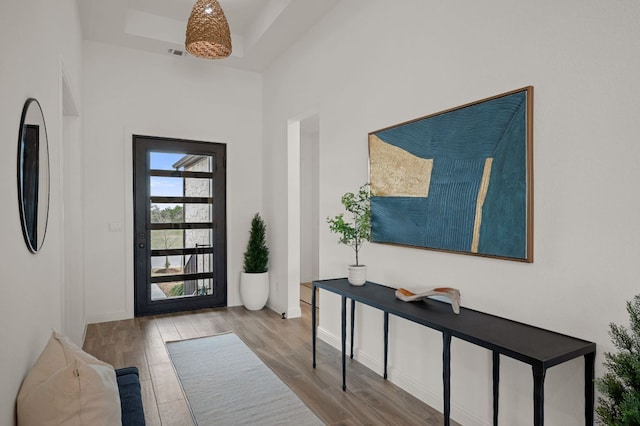 entryway with visible vents, baseboards, a tray ceiling, and wood finished floors