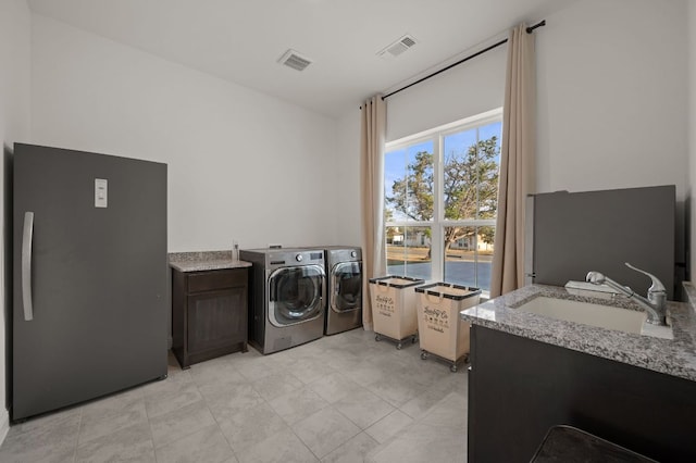 laundry area featuring separate washer and dryer, visible vents, cabinet space, and a sink