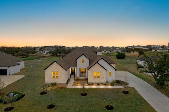 french country inspired facade with stone siding, driveway, a front lawn, and board and batten siding