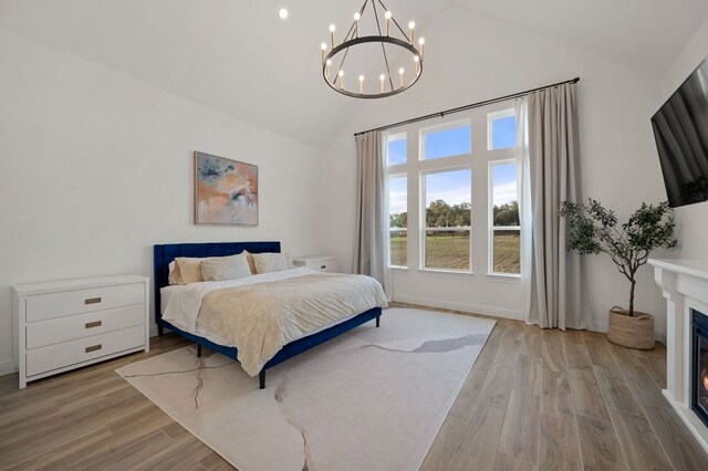 bedroom with a notable chandelier, high vaulted ceiling, a glass covered fireplace, and wood finished floors