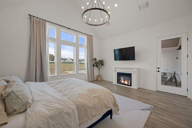 bedroom with visible vents, a notable chandelier, high vaulted ceiling, a glass covered fireplace, and wood finished floors