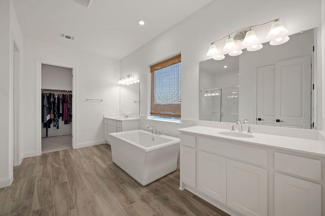 full bath with visible vents, a shower stall, two vanities, wood finished floors, and a sink