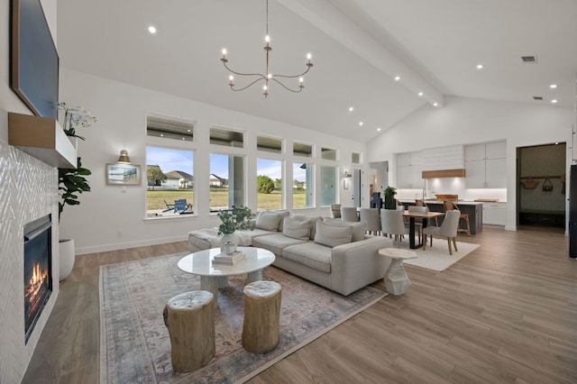 living room featuring light wood finished floors, a chandelier, beam ceiling, a fireplace, and high vaulted ceiling