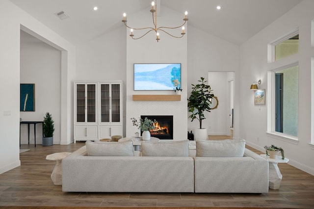 living room with visible vents, high vaulted ceiling, wood finished floors, and a glass covered fireplace