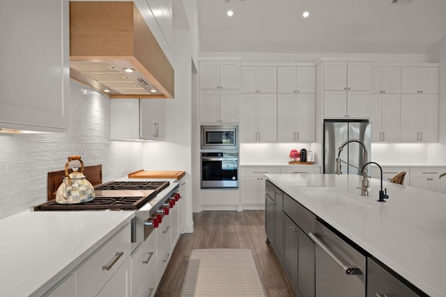 kitchen featuring custom range hood, a sink, appliances with stainless steel finishes, white cabinets, and light countertops