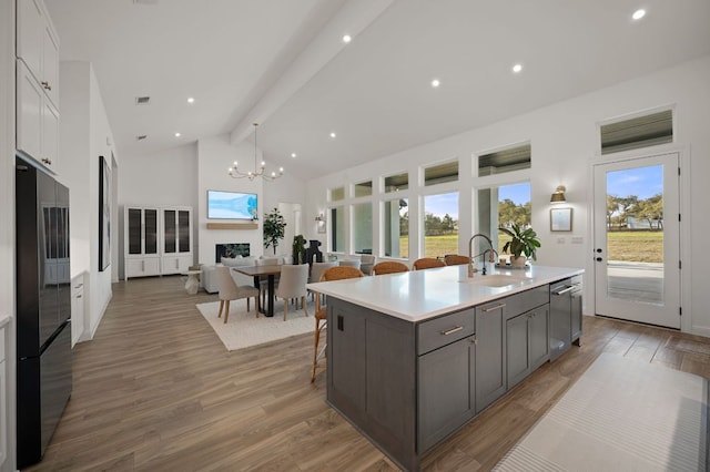 kitchen with beam ceiling, high vaulted ceiling, a sink, freestanding refrigerator, and light wood-style floors