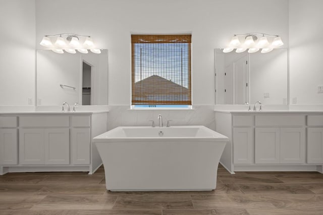 full bathroom featuring a freestanding tub, two vanities, wood finish floors, and a sink