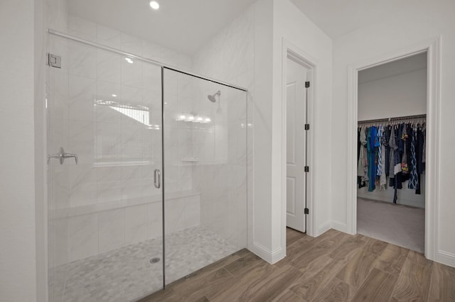 bathroom with a stall shower, a walk in closet, and wood finished floors