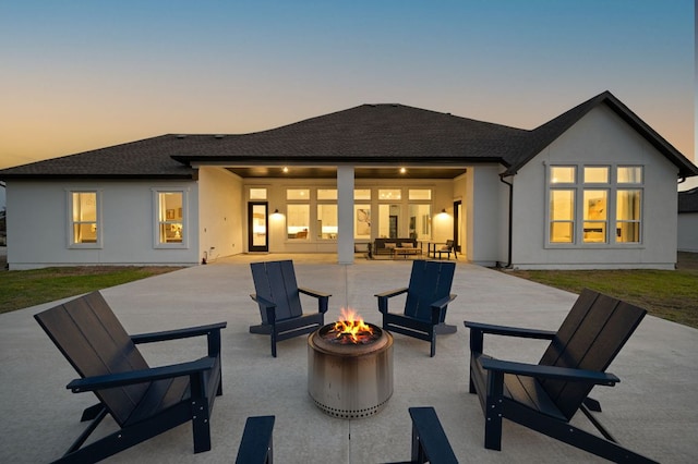 back of house at dusk with a patio area, stucco siding, a fire pit, and a shingled roof