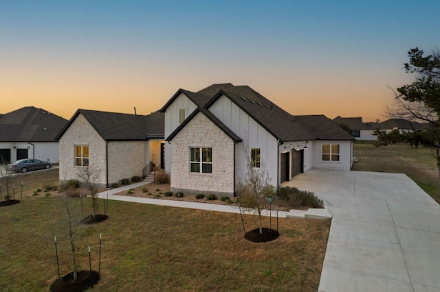 modern farmhouse with a front lawn, stone siding, board and batten siding, concrete driveway, and a garage