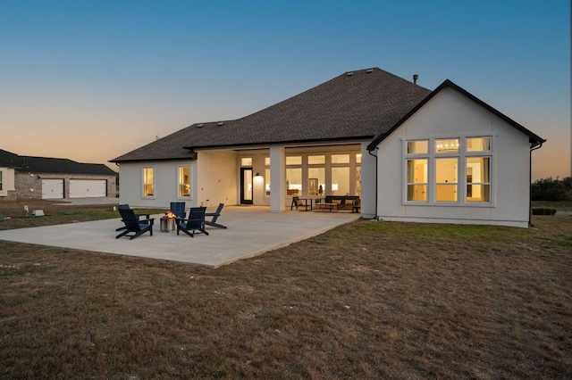 back of house with a fire pit, a shingled roof, stucco siding, a lawn, and a patio