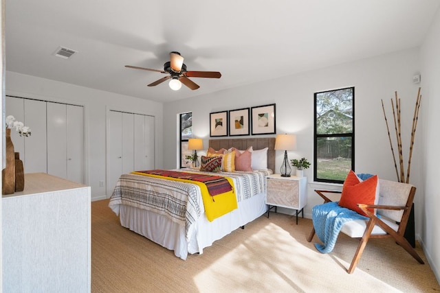 bedroom featuring a ceiling fan, visible vents, two closets, and light carpet