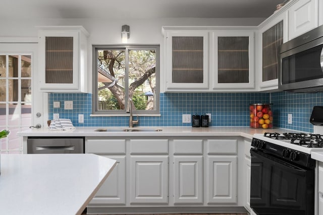 kitchen with light countertops, decorative backsplash, appliances with stainless steel finishes, white cabinets, and a sink