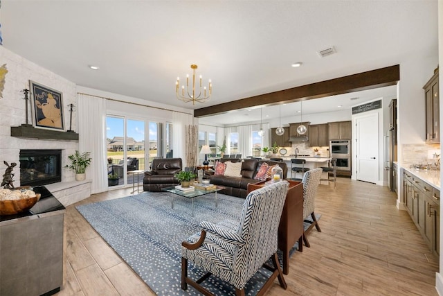 living area featuring visible vents, recessed lighting, a stone fireplace, light wood-style floors, and a chandelier