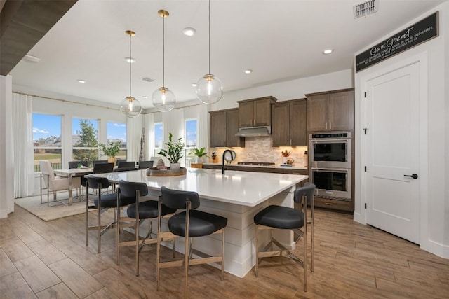 kitchen with visible vents, under cabinet range hood, gas cooktop, tasteful backsplash, and double oven