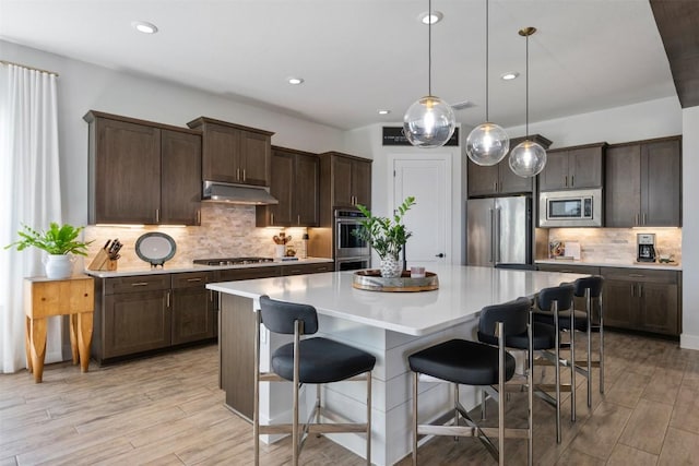 kitchen with under cabinet range hood, stainless steel appliances, a kitchen island, and dark brown cabinetry