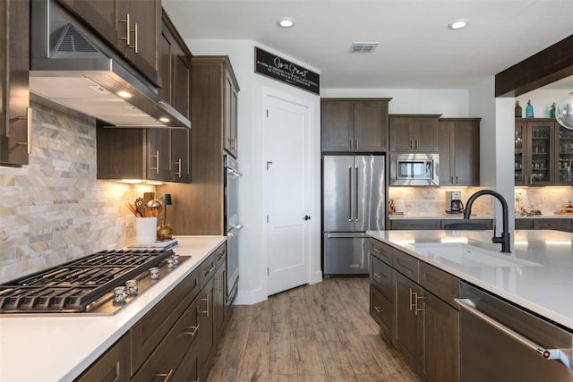 kitchen with visible vents, under cabinet range hood, dark brown cabinetry, stainless steel appliances, and a sink