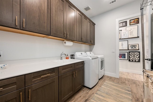 laundry area with visible vents, light wood-style flooring, a sink, cabinet space, and washing machine and clothes dryer