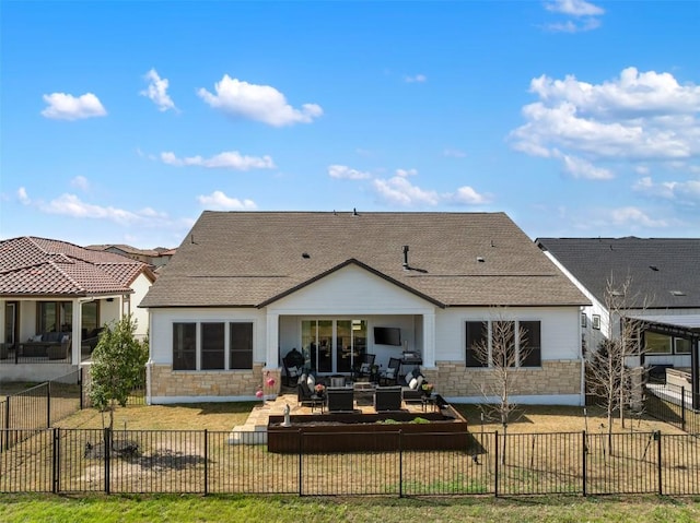 back of property with a fenced front yard, stone siding, a patio, and a shingled roof