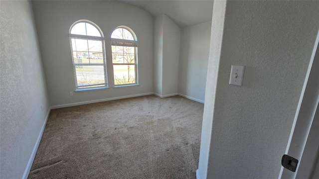 carpeted empty room with baseboards, vaulted ceiling, and a textured wall