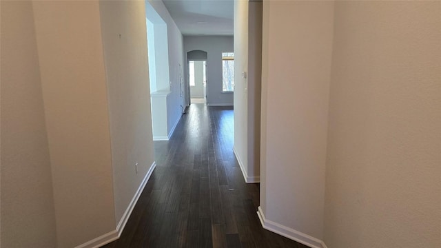 corridor with dark wood finished floors, baseboards, and arched walkways