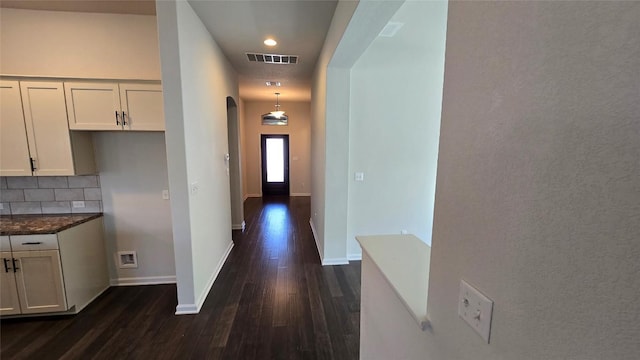 corridor featuring baseboards, dark wood-style floors, visible vents, and arched walkways