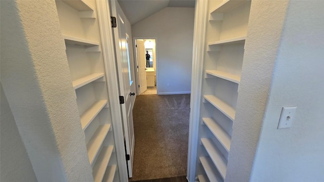 corridor featuring built in shelves, baseboards, lofted ceiling, and dark colored carpet