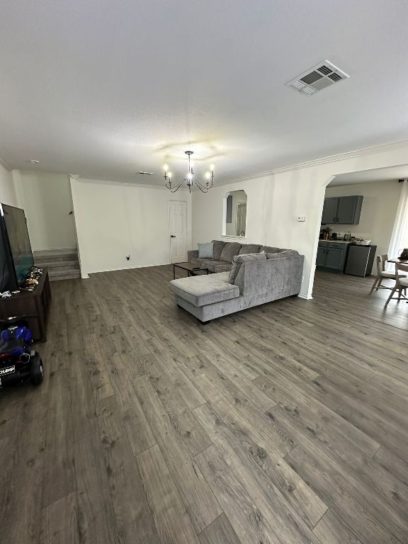 living area featuring visible vents, a notable chandelier, dark wood finished floors, arched walkways, and crown molding