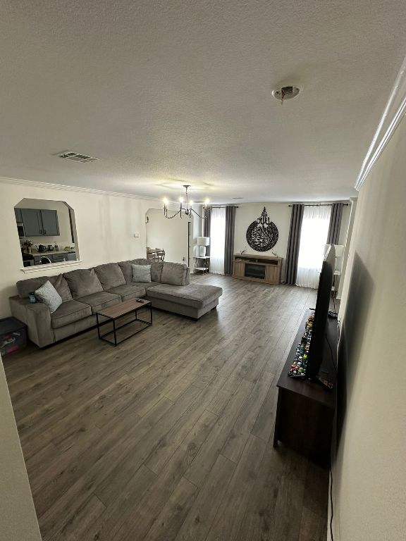 living area featuring visible vents, dark wood-type flooring, a chandelier, ornamental molding, and a textured ceiling