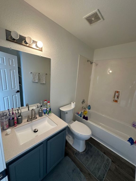 full bath with visible vents, toilet, a textured wall, vanity, and  shower combination