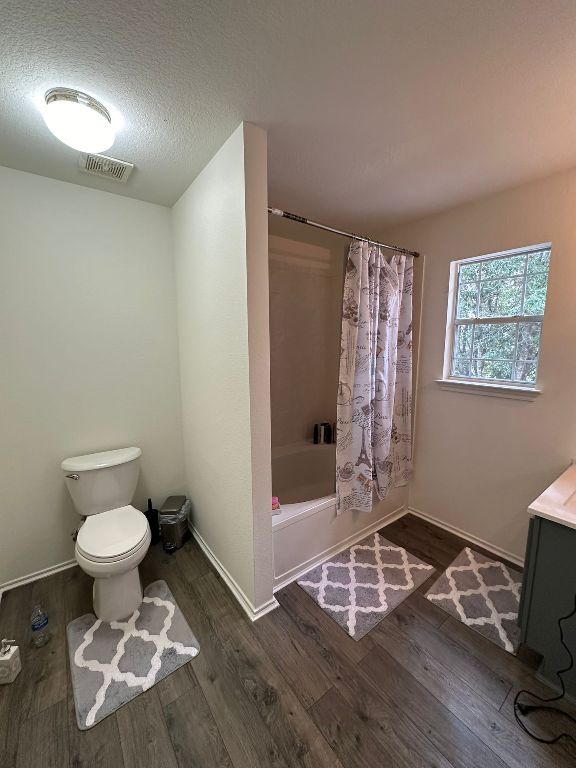 full bathroom with visible vents, toilet, shower / bath combo, wood finished floors, and a textured ceiling