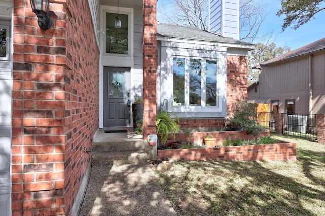 view of exterior entry featuring fence, brick siding, roof with shingles, and a chimney