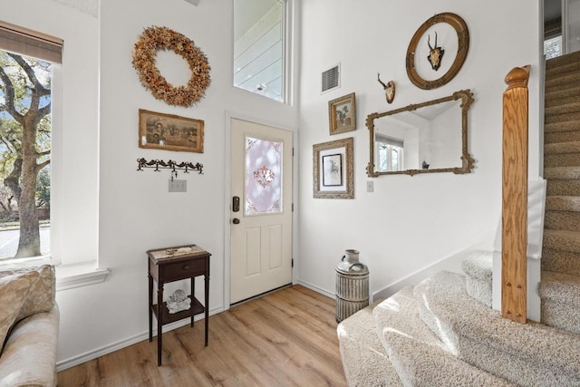 foyer entrance with light wood finished floors, visible vents, stairs, and baseboards